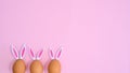Three natural eggs with rabbit ears peek on pastel pink background with copy space. Easter flat lay minimal Royalty Free Stock Photo
