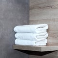 Three neatly folded white towels lie on a wooden shelf against a background of ceramic tiles.