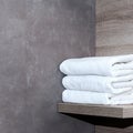 Three neatly folded white towels lie on a wooden shelf against a background of ceramic tiles