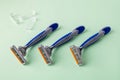 Three new disposable shaving razors with triple blade lie in a row on a pastel green background. Silver blue plastic razor with Royalty Free Stock Photo