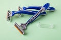 Three new disposable shaving razors with triple blade on a pastel green background. Silver blue plastic razor with orange lubricat Royalty Free Stock Photo