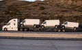 Three new white vans being transported on a flatbed truck in afternoon light