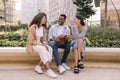 Three nice young interracial guys and girls are having discussing their homework sitting on street.