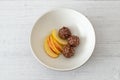 Three Nutty Clustered Chocolate Ice Cream Balls and Sliced Apple in a brown Serving Bowl on White Painted Wooden Boards