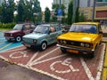 Three old cars parked on the disability parking lot. One is purple, one is blue, and the last one is yellow