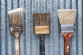 Three Old Dirty Crusty Household Paintbrushes on Shiny Corrugated Metal Background
