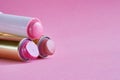 Three old used lipstick tubes lie on a pink background