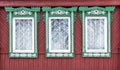 Three old windows with grilles and carved wooden green-white architraves on red wall from board. Royalty Free Stock Photo