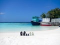 Three pairs of flip flops sandals on a Maldive beach propped up in the sand with an old fishing boat at a quay behind and palm tre Royalty Free Stock Photo