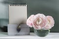 Three pale pink ranunculus in transparent round vase on the white windowsill. album on springs in a box for paper. Copy space.