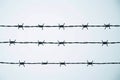 Three parallel strands of barbed wire set against a pale blue sky, conveying themes of restriction and isolation Royalty Free Stock Photo