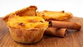 Three Pastel de nata or Portuguese egg tart and cinnamon sticks on a wooden brown background. Pastel de Belem is a small