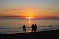 Three peolple walking on a beach under sunset Royalty Free Stock Photo