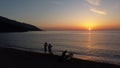 Three people on the beach meet the sunset