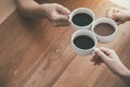 Three people clinking coffee cups on wooden table in cafe