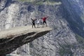 Three people family holding hands on Trolltunga rock formation. Jutting cliff is in Odda, Hordaland county, Norway