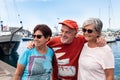 Three people friends stay together on pier looking at beautiful port and boats. Senior male and females. Summer day of vacations