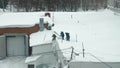 Three people throw snow off the roof