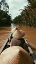 Three people wearing Asian conical hats in a small wooden boat rowing down a river Royalty Free Stock Photo