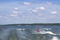 Three Personal Watercraft jump wakes on a lake with trees and houses on shoreline in the distance under a blue sky with clouds