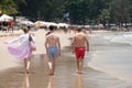 Three persons - women, man and younger guy between them walk on sand beach along the water. Sunny tropical day at Bang Thao beach