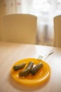 Three pickled cucumbers in an orange plate with a fork on the kitchen table Royalty Free Stock Photo
