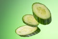 Three pieces of cucumber hang arbitrarily on a green background with a gradient. Royalty Free Stock Photo