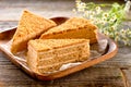 Three pieces of honey cake with wooden platter and field camomile flowers on textured boards background Royalty Free Stock Photo