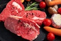 Three pieces of juicy raw beef with vegetables on a stone cutting board on a black wooden table background Royalty Free Stock Photo