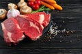 Three pieces of juicy raw beef with vegetables on a stone cutting board on a black wooden table background Royalty Free Stock Photo