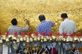 Three Pilgrims pasting gold foils leaves together onto golden rock at the Kyaiktiyo Pagoda with small bells in foreground