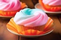 three pink blue cotton candy cupcakes in orange cupcake liners on tiny plates. blurred background.