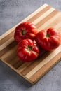 Three pink heirloom tomato vegetables, fresh red ripe tomatoes on wooden cutting board, vegan food