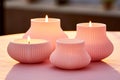 Three pink round coral-hued candles with a pleated design, glowing warmly at dusk, arranged on a blurred surface, evoke