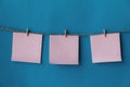 Three pink sheets of paper with place for text hanging on rope isolated blue background. To do list. Pink sticky notes with cloth