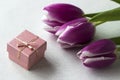 Three pink tulips with a white border on the petals lie on the table with a small pink gift box, background. Holiday concept Royalty Free Stock Photo