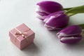 Three pink tulips with a white border on the petals lie on the table with a small pink gift box, background. Holiday concept Royalty Free Stock Photo