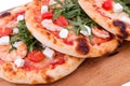 Three pizzas with prawns, tomatoes, arugula and cheese on a wooden background