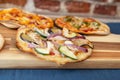 Three pizzas on a wooden board, fresh out of the oven. Focus on vegetable pizza