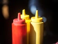 Three plastic bottles, red and yellow, used for fast food sauces such as ketchup and mustard, on display on a restaurant table Royalty Free Stock Photo