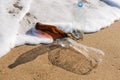 Three plastic bottles stand and lie on the seashore, white foam and yellow sand, pollution concept of nature Royalty Free Stock Photo