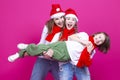 Three Positive Caucasian Girls With Santa Hats Having Fun While Lifting Teenage Girl Holding Hands Closed Against Trendy Pink Royalty Free Stock Photo