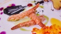 Three prawns on a white table decorated with chopped vegetables and sauce.