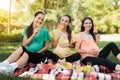 Three pregnant women posing in a picnic park with large colored candies