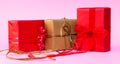 Three presents, red and kraft, with simple different material bows and pink background. Horizontal