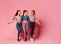 Three pretty athletic girls in high-tech modern colorful sportswear vigorously walk together towards their health on pink