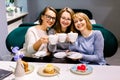 Three pretty Caucasian girl friends spend time together drinking coffee in the cafe, having fun and eating cakes and Royalty Free Stock Photo