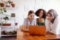 Three pretty female teenagers of different nationalities are looking at the laptop screen and laughing Royalty Free Stock Photo