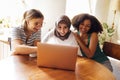 Three pretty female teenagers of different nationalities are looking at the laptop screen and laughing Royalty Free Stock Photo