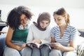 Three pretty female teenagers of different nationalities are reading a magazine and smiling Royalty Free Stock Photo
